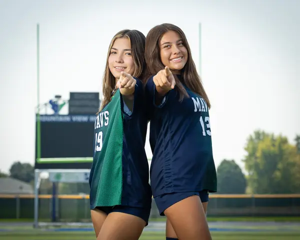 Maria Rojas #19 and Alexa Martinez #13 in a horizontal frame, shoulder to shoulder, both pointing at the camera