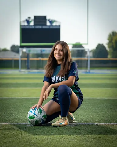 Alexa Martinez #13 full length, kneeling with a hand on the ball, scoreboard and goalposts behind her
