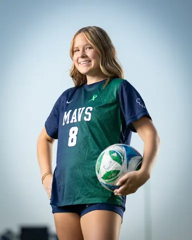 Allie Louvier #8 waist up from a low angle, smiling with the ball at her hip against a pale sky