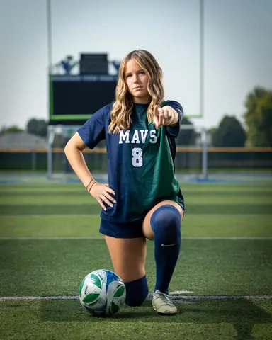 Allie Louvier #8 full length, kneeling beside the ball and pointing at the camera