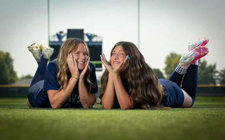 Allie Louvier #8 and Vivian Sipe #9 lying on the turf, chins in their hands, cleats in the air