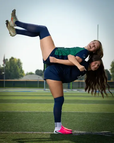 Vivian Sipe #9 hoisting Allie Louvier #8 across her back, Allie's cleats kicked high, both laughing