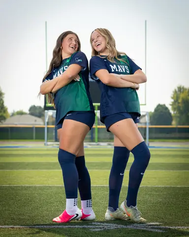 Vivian Sipe #9 and Allie Louvier #8 back to back with arms crossed, laughing at each other