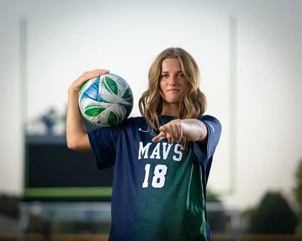 Kora De Burgh #18 waist up, ball on her shoulder, pointing at the camera