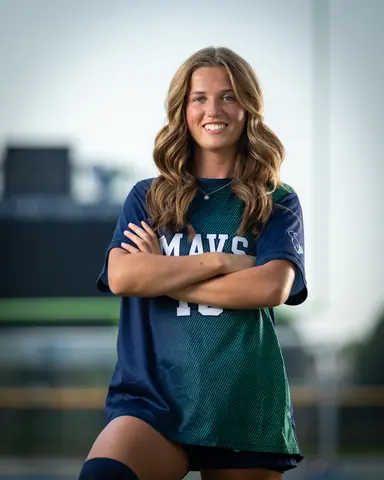 Kora De Burgh #18 from the waist up, arms crossed and smiling on the Mountain View field