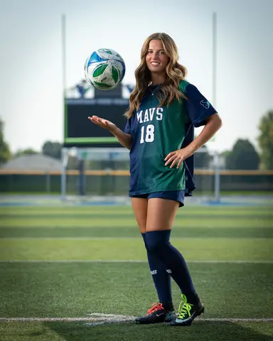 Kora De Burgh #18 full length on the field, tossing the ball up from an open palm, hand on hip