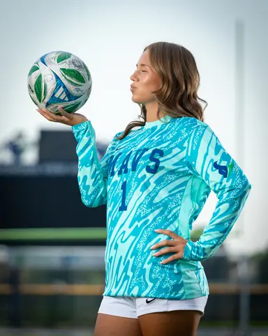 Laney Otero #1 waist up in profile in her keeper jersey, eyes closed and lips puckered, ball on her palm