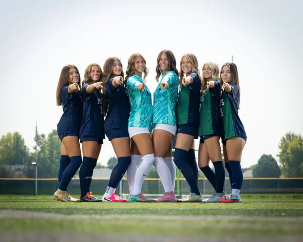 The eight Mountain View girls soccer seniors smiling and pointing at the camera, keepers in teal at center