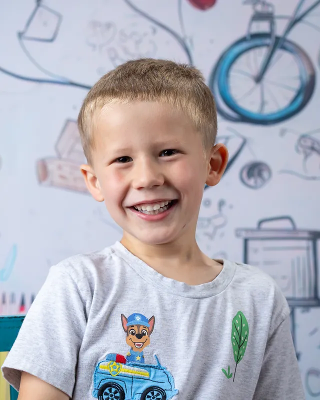 Big-smile headshot of a preschool boy against a hand-drawn school backdrop at daycare picture day - daycare photographer Meridian Idaho