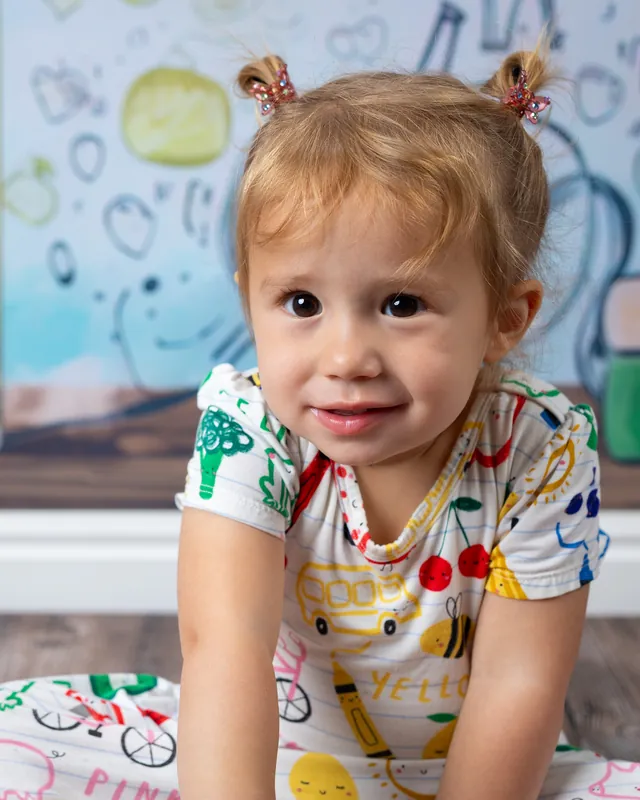 Toddler girl with pigtails smiling at the camera on the floor at daycare picture day - daycare photographer Meridian Idaho