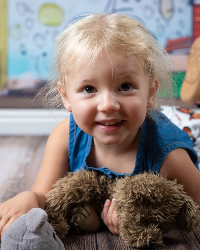 Toddler lying on the floor grinning with her stuffed animals at daycare photo day - daycare photographer Meridian Idaho