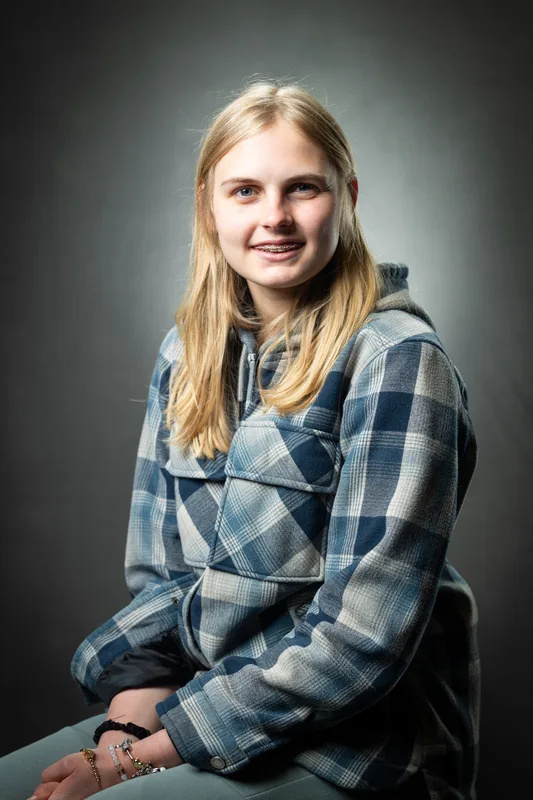 Seated school photo day portrait of an older student in a plaid flannel on a grey studio backdrop - high school photography Treasure Valley Idaho