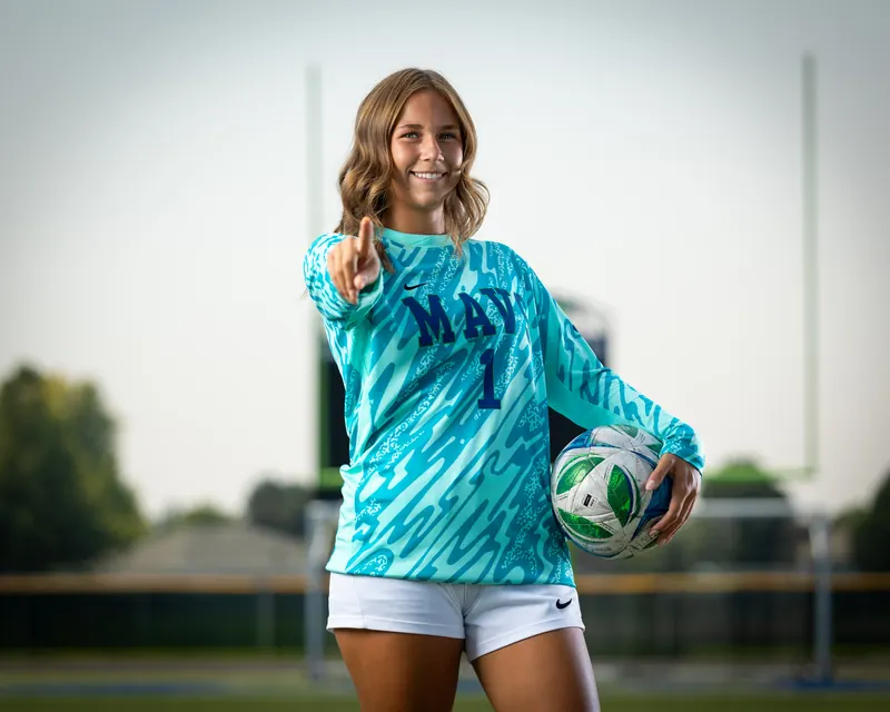 Mountain View High School girls soccer goalkeeper in a teal jersey pointing at the camera with a ball on her hip, Meridian, Idaho