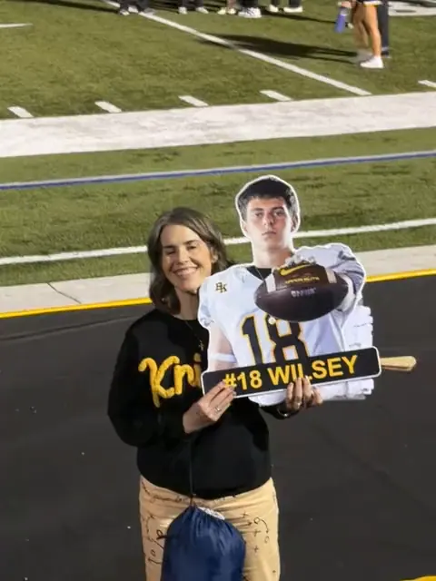 A Bishop Kelly mom on the field holding her son's plated torso cutout reading #18 Wilsey