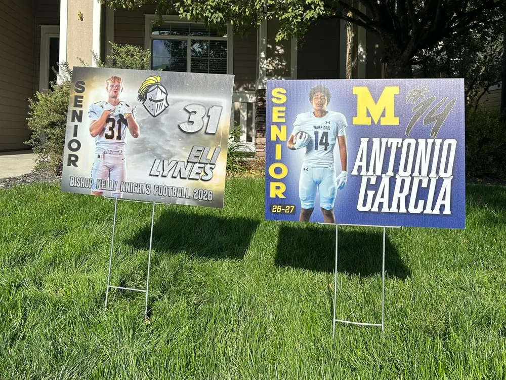 Two custom senior football yard signs on H-stakes in a front lawn: Eli Lynes #31 for Bishop Kelly Knights and Antonio Garcia #14 for the Meridian Warriors