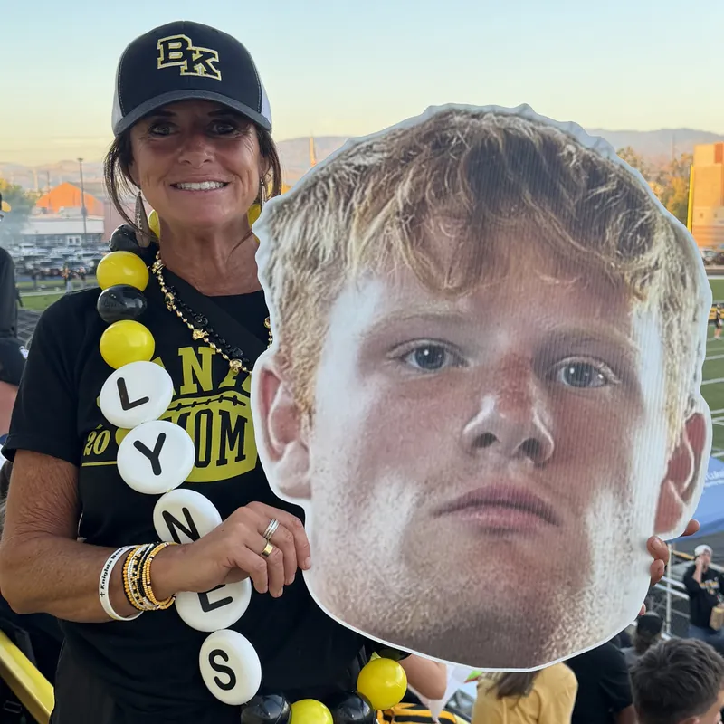 Michelle Lynes in the Bishop Kelly stands on game night, holding up a big head cutout of a player